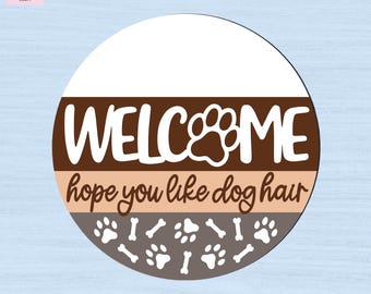 May include: A circular sign featuring a white top section, a brown middle band with the white text WELCOME and a paw print, a light tan band with the brown text hope you like dog hair, and a dark brown bottom section with white paw prints and bones.