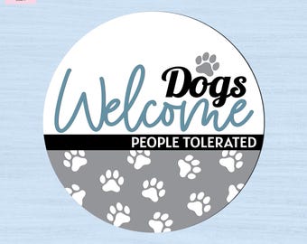 May include: A circular sign featuring the text Welcome Dogs in blue and black script and print, with a black horizontal bar containing the white text PEOPLE TOLERATED. The bottom section is gray with a repeating pattern of white paw prints.