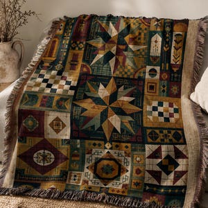 May include: A woven throw blanket featuring a multi-coloured geometric pattern with prominent star motifs, checkered squares, and intricate line work in shades of mustard yellow, deep teal, burgundy, and cream, finished with a fringed edge.