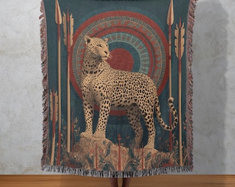 May include: A teal throw blanket featuring a detailed illustration of a leopard standing on a rock. The design includes spears, a circular pattern, and a fringed edge. The leopard has a spotted coat and is set against a teal background.