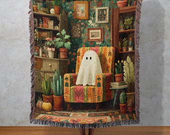 Puede incluir: Una manta tejida que presenta una ilustración caprichosa de un fantasma sentado en un sillón estampado en una habitación acogedora llena de plantas, libros y obras de arte. La manta tiene un borde con flecos y una cálida paleta de colores verdes, naranjas y marrones.