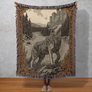 May include: A woven throw blanket with a detailed illustration of a wolf howling in a forest, with a castle in the background. The blanket has a decorative border and fringe.