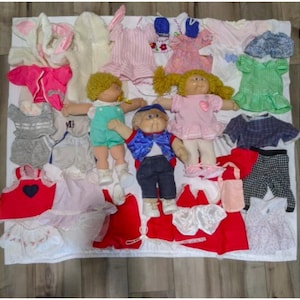 May include: A collection of Cabbage Patch Kids dolls and clothing. The dolls are wearing a variety of outfits, including dresses, shirts, and pants. There are also several accessories, such as hats, shoes, and purses.
