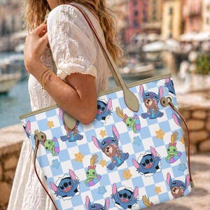 May include: A light blue and white checkered tote bag featuring cartoon characters. The bag has brown handles and a light brown trim. The cartoon characters are blue with large ears and are set against a background of yellow flowers.