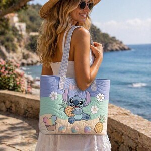 May include: A beach-themed quilted tote bag. The bag features a cartoon character holding a pineapple, with seashells, flowers, and a cupcake graphic. The bag has a light blue, green, and tan colour scheme with a checkered strap.