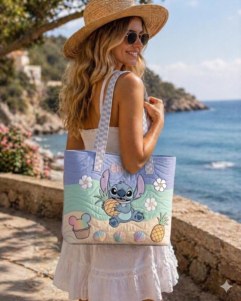 May include: A beach-themed quilted tote bag. The bag features a cartoon character holding a pineapple, with seashells, flowers, and a cupcake graphic. The bag has a light blue, green, and tan colour scheme with a checkered strap.