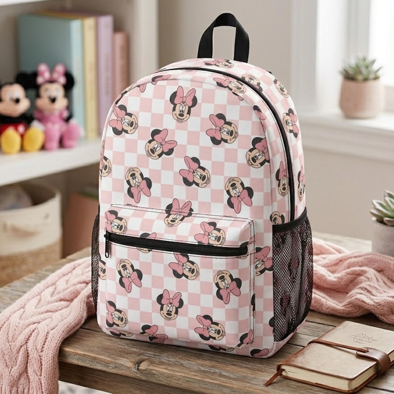 Peut inclure: Un sac &agrave; dos avec un motif r&eacute;p&eacute;titif de visages de Minnie Mouse avec des n&oelig;uds roses sur un fond &agrave; carreaux rose clair et blanc. Le sac comprend une poign&eacute;e sup&eacute;rieure, une poche avant zipp&eacute;e et des poches lat&eacute;rales en filet noir.