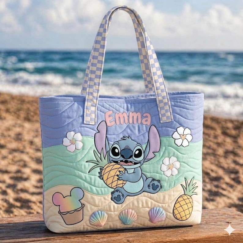 May include: A quilted tote bag with a cartoon character holding a pineapple. The bag has a light blue background with a wave pattern, white flowers, and the name "Emma". The handles and top trim have a checkered pattern.