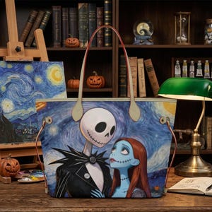 Puede incluir: Un bolso tote con un estampado gr&aacute;fico de Jack Skellington y Sally de Pesadilla antes de Navidad sobre un fondo azul de noche estrellada. El bolso cuenta con dos asas de hombro de color claro y herrajes de metal en tono dorado.