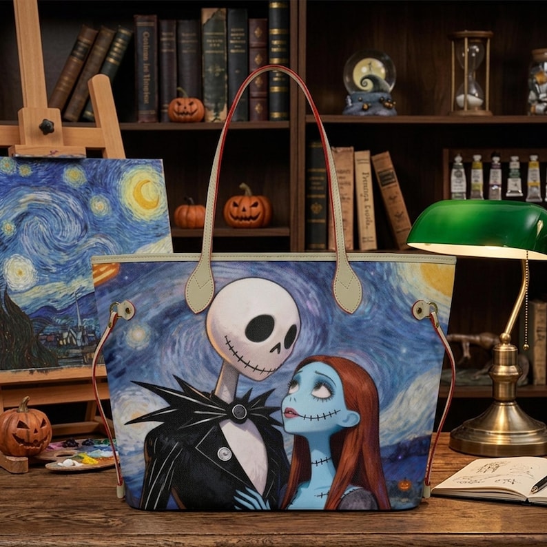Puede incluir: Un bolso tote con un estampado gr&aacute;fico de Jack Skellington y Sally de Pesadilla antes de Navidad sobre un fondo azul de noche estrellada. El bolso cuenta con dos asas de hombro de color claro y herrajes de metal en tono dorado.