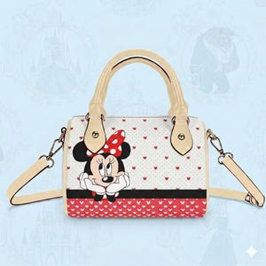 May include: A white handbag featuring Minnie Mouse with a red polka dot bow. The bag has a cream-colored handle and strap, with a red heart pattern on the bottom and a black stripe. The bag is approximately 9 inches wide.