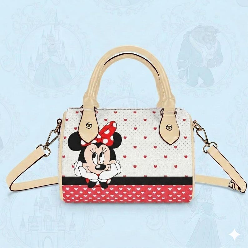 May include: A white handbag featuring Minnie Mouse with a red polka dot bow. The bag has a cream-colored handle and strap, with a red heart pattern on the bottom and a black stripe. The bag is approximately 9 inches wide.