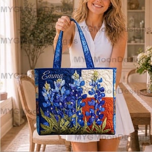Puede incluir: Un bolso tote acolchado con un diseño floral de altramuces y la bandera del estado de Texas. El bolso tiene asas azules y el nombre "Emma" bordado en la parte delantera. El bolso es una mezcla de azul, blanco, rojo y verde.