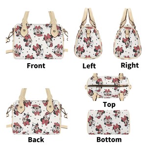 Op de afbeelding: Een witte handtas met een patroon van Minnie Mouse-illustraties met rode strikken en zwarte stippen. De tas heeft beige handvatten en afwerking, een ritssluiting en een afneembare schouderriem.