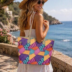 May include: A tote bag featuring a colourful patchwork pattern of purple, orange, yellow, and blue sections with various prints including swirls, stripes, and polka dots, held by two light-coloured shoulder straps with metallic hardware accents.
