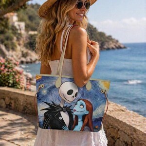 Puede incluir: Un bolso tote rectangular con un estampado gr&aacute;fico de Jack Skellington y Sally de Pesadilla antes de Navidad sobre un fondo azul de noche estrellada. El bolso cuenta con dos asas finas de color claro y herrajes en tono dorado.