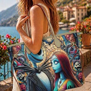 May include: A large tote bag featuring a colorful stained glass style print of Jack Skellington and Sally. The design includes intricate patterns of roses, skulls, and bats in shades of blue, red, and yellow. The bag has light beige straps and trim.