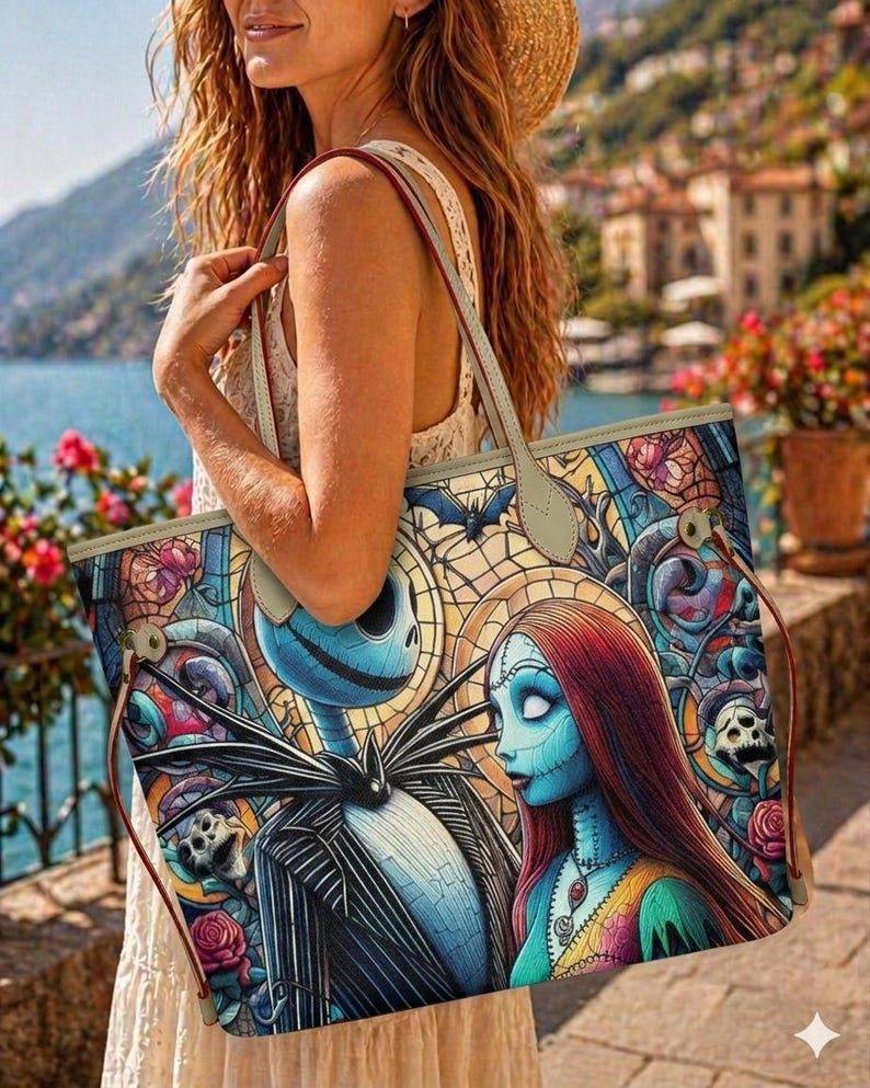 May include: A large tote bag featuring a colorful stained glass style print of Jack Skellington and Sally. The design includes intricate patterns of roses, skulls, and bats in shades of blue, red, and yellow. The bag has light beige straps and trim.