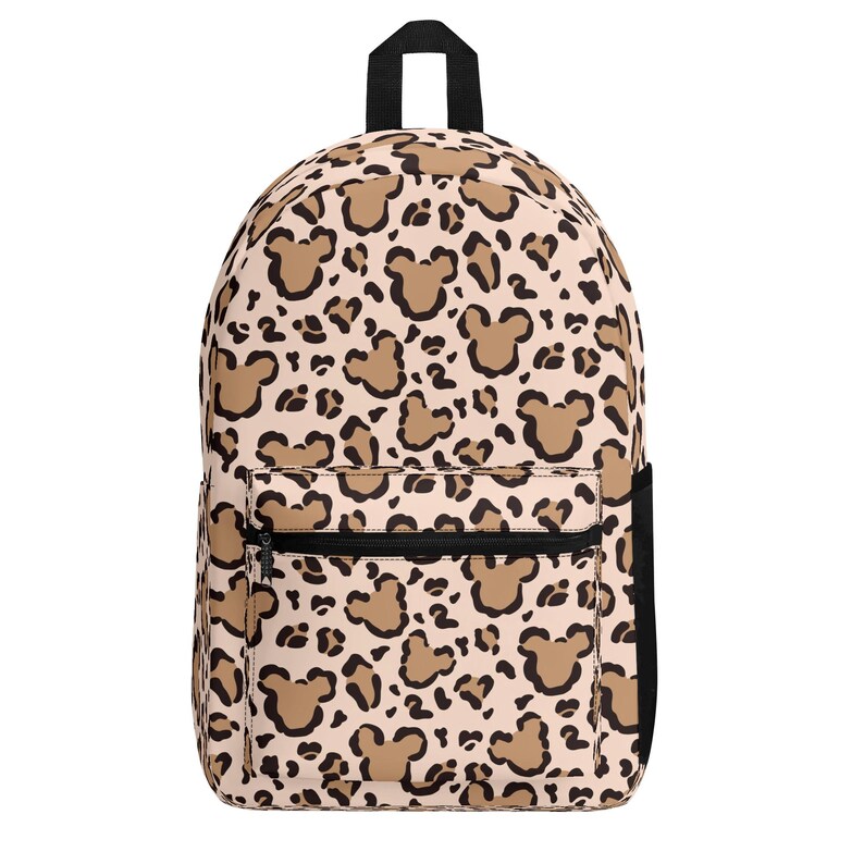 May include: A backpack featuring a light beige background with a repeating animal print pattern that incorporates dark brown mouse-ear silhouettes. The bag includes a top handle, a front zippered pocket, and a black side pocket on the right side.