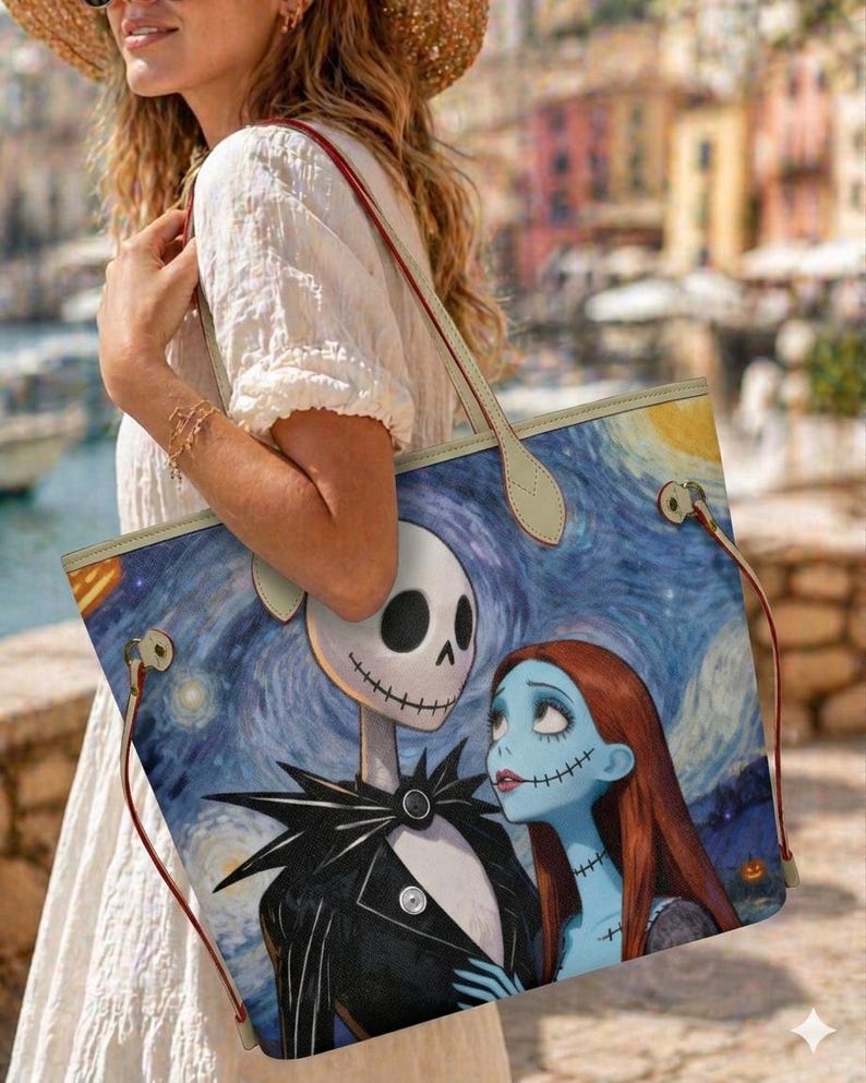 Puede incluir: Un bolso tote con una ilustraci&oacute;n impresa de Jack Skellington y Sally sobre un fondo azul de noche estrellada. El bolso tiene asas de color claro con bordes rojos y herrajes met&aacute;licos en los laterales para sujetar las correas.