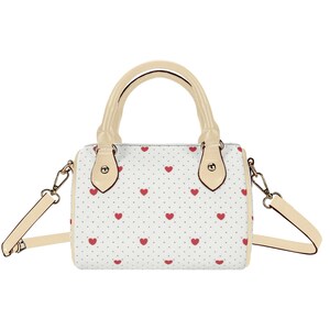 May include: A white handbag with a pattern of small red hearts and gray dots. The bag has a cream-colored handle and shoulder strap. The hardware is gold-colored.
