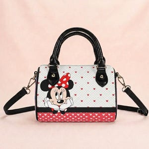May include: A white and red Minnie Mouse handbag with black handles and a black shoulder strap. The bag features a Minnie Mouse graphic, red heart patterns, and a red and white polka dot bow. The bag has a rectangular shape.