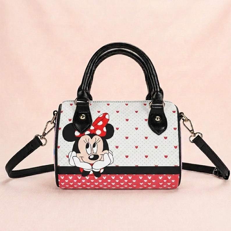 May include: A white and red Minnie Mouse handbag with black handles and a black shoulder strap. The bag features a Minnie Mouse graphic, red heart patterns, and a red and white polka dot bow. The bag has a rectangular shape.