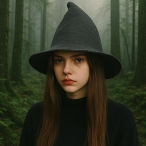 May include: A dark gray witch hat with a wide brim and a pointed crown. The hat is worn with a black turtleneck sweater. The background is a misty forest with tall green trees.