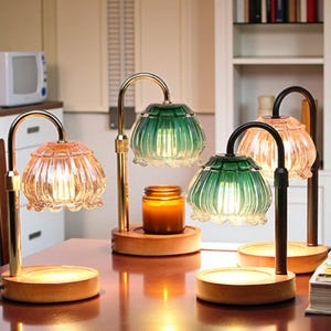 Op de afbeelding: Vier decoratieve tafellampen met glazen kappen in groen- en amberkleuren. De lampen hebben een houten voet en een gebogen metalen arm. Een kaars staat tussen twee van de lampen.