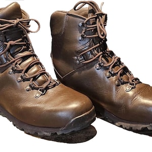 Può includere: Un paio di scarponi da trekking in pelle marrone con lacci marrone scuro e occhielli in metallo. Gli scarponi hanno un design a stelo alto e una suola robusta, adatti alle attività all'aperto. Gli scarponi sono mostrati su sfondo bianco.