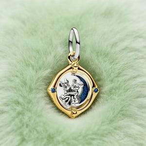 May include: A gold-coloured pendant with a silver bail, depicting Mickey and Minnie Mouse embracing on a crescent moon. The pendant is diamond-shaped with blue accents and star details, set against a soft green background.