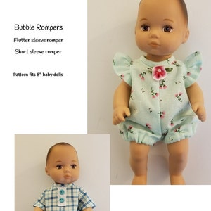 Puede incluir: Dos muñecas bebés que llevan diferentes mamelucos. La muñeca de la izquierda lleva un mameluco a cuadros azul y blanco con mangas cortas. La muñeca de la derecha lleva un mameluco azul claro con estampado floral y mangas de volantes. El texto "Bubble Rompers" está en la parte superior de la imagen. El texto "Flutter sleeve romper" y "Short sleeve romper" está debajo del título. El texto "Pattern fits 8" baby dolls" está debajo de las descripciones de los mamelucos. El texto "Kathy Anne Designs for dolls" está en la parte inferior de la imagen.
