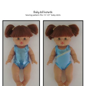 Op de afbeelding: Twee babypoppen met blauwe turnpakjes. De poppen hebben bruin haar in staartjes en zijn ontworpen voor 34,3 cm babypoppen. De tekst op de afbeelding luidt "Baby doll leotards" en "Kathy Anne Designs for dolls."