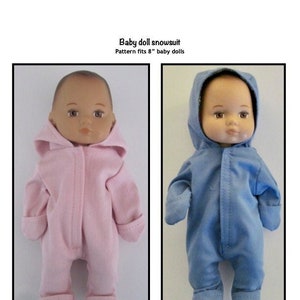 May include: Two baby dolls wearing snowsuits. The doll on the left is wearing a pink snowsuit and the doll on the right is wearing a blue snowsuit. Both dolls have brown hair and brown eyes. The text "Baby doll snowsuit" and "Pattern fits 8" baby dolls" is printed above the dolls. The text "Kathy Anne Designs for dolls" is printed below the dolls.