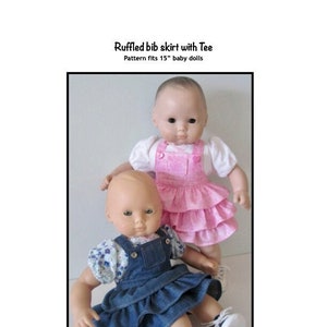 May include: Two 15-inch baby dolls wearing ruffled bib skirts. The doll on the left is wearing a blue denim skirt with a white floral print shirt. The doll on the right is wearing a pink ruffled skirt with a white short-sleeved shirt. The text "Ruffled bib skirt with Tee" and "Pattern fits 15" baby dolls" is above the dolls. The text "Kathy Anne Designs for dolls" is below the dolls.