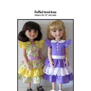 May include: Two dolls wearing ruffled tiered dresses. The doll on the left is wearing a yellow dress with floral print and a pink sash. The doll on the right is wearing a purple dress with white polka dots and a white sash. Both dolls are wearing black shoes. The text "Ruffled tiered dress" and "Pattern fits 15" slim dolls" is printed above the dolls. The text "Kathy Anne Designs for dolls" is printed below the dolls.