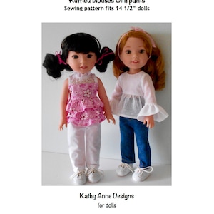 May include: Two dolls wearing ruffled blouses and pants. The doll on the left is wearing a pink and white floral blouse and white pants. The doll on the right is wearing a white blouse with a ruffled hem and blue jeans. Both dolls are wearing white shoes. The text "Ruffled blouses with pants Sewing pattern fits 14 1/2" dolls" is at the top of the image. The text "Kathy Anne Designs for dolls" is at the bottom of the image.