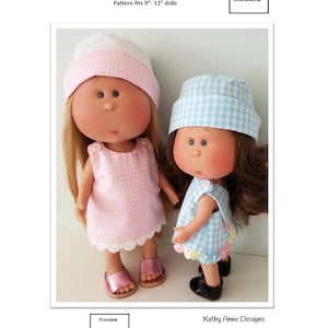 May include: Two dolls wearing cross back dresses, bloomers, and hats. One doll wears a pink gingham set with a white hat, the other a blue gingham set with a matching hat. Text reads: Cross back dress, bloomer and hat, Pattern fits 9-11 inch dolls, 2 sizes included, Printable PDF Pattern, Kathy Anne Designs for dolls.