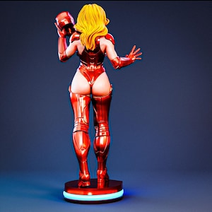 May include: A collectible figurine of a character with long blonde hair, wearing a metallic red bodysuit with matching armor plates on the shoulders, arms, and legs. The figure holds a red helmet in one hand and stands on a circular base with light.
