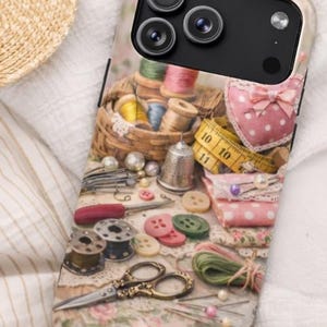 Może przedstawiać: Etui na telefon z kolażem akcesoriów do szycia. Projekt zawiera szpulki nici, guziki, nożyczki, naparstek i miarkę. Paleta kolorów jest delikatna, z różami, zielenią i żółciami.