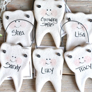 May include: Six white ceramic tooth ornaments with painted faces and names, including "Shea", "Sandy", "Lucy", "Lisa", "Tracy", and "Growing Smiles".