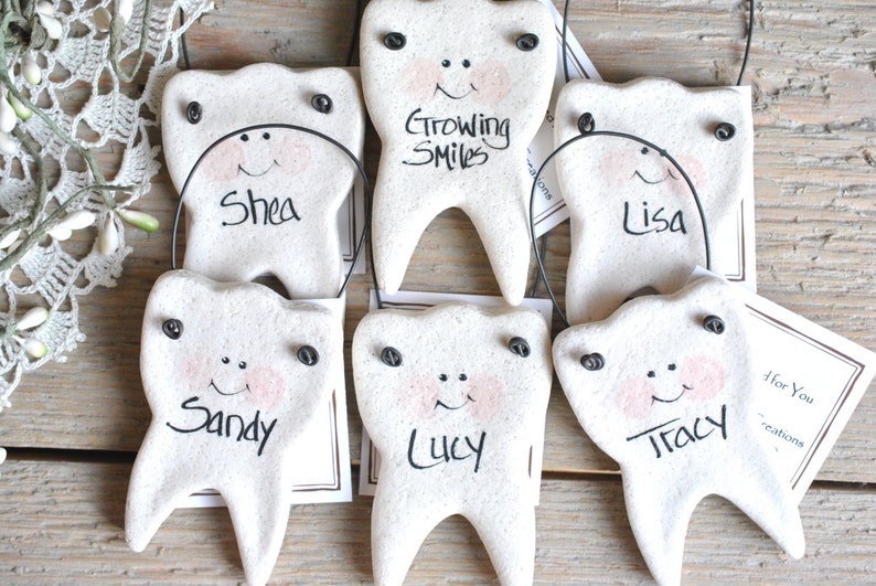 May include: Six white ceramic tooth ornaments with painted faces and names, including "Shea", "Sandy", "Lucy", "Lisa", "Tracy", and "Growing Smiles".