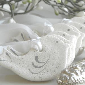 May include: A set of white ceramic dove ornaments with gray painted details. Each dove has a white satin ribbon attached for hanging.