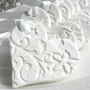 May include: A row of white heart-shaped ornaments with a decorative floral design. The ornaments are tied with white ribbon and are perfect for a wedding or other special occasion.