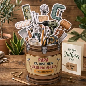 May include: A decorative toolbox filled with paper cutouts of various tools, including a drill, saw, and level. The toolbox has a label that reads "PAPA DU BIST MEIN LIEBLING SHELD" and "DANKE FÜR ALLES!" A Father's Day card is also present.