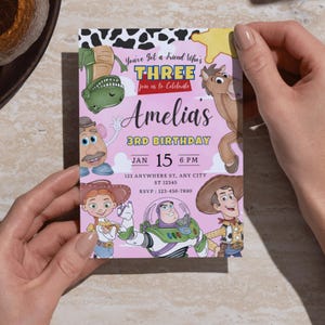 Puede incluir: Una tarjeta de invitaci&oacute;n de cumplea&ntilde;os rectangular con fondo rosa claro y personajes de dibujos animados. El texto dice: You've Got a Friend Who's THREE join us to Celebrate Amelia's 3RD BIRTHDAY JAN 15 6 PM 123 ANYWHERE ST, ANY CITY ST 12345 RSVP: 123-456-7890.