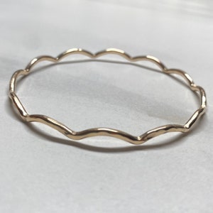 May include: A gold-toned bangle bracelet with a wavy, scalloped design.