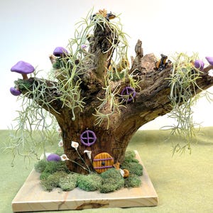 May include: A miniature fairy house made from a tree branch with purple mushrooms, green moss, and a small wooden door. The house is decorated with small, purple flowers and a yellow wheel.