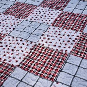 May include: A patchwork quilt with a variety of patterns, including red and black plaid, white with a small red design, and a solid light blue. The quilt is quilted with a diamond pattern.