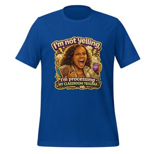 May include: A royal blue t-shirt featuring a graphic illustration of a person with curly hair shouting, holding a stack of books and a purple mug. The text reads, I'm not yelling, I'm processing MY CLASSROOM TRAUMA, surrounded by yellow lightning bolts.
